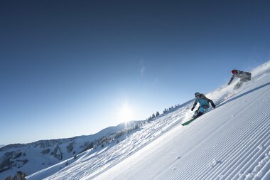 Zwei Skifahrer genießt die verschneiten Hänge am Hochkönig unter strahlendem Sonnenschein.  | © Hochkönig Tourismus GmbH
