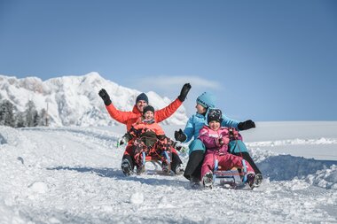Familie beim winterlichen Rodeln in der Region Hochkönig. Strahlender Sonnenschein und verschneite Berglandschaft erleben. | © Hochkönig Tourismus GmbH
