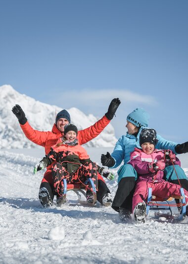 Familie beim winterlichen Rodeln in der Region Hochkönig. Strahlender Sonnenschein und verschneite Berglandschaft erleben. | © Hochkönig Tourismus GmbH