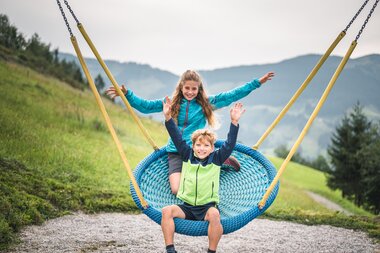 Kinder genießen eine Schaukel im Hochkönig, umgeben von grünen Wiesen und Bergen.  | © Hochkönig Tourismus GmbH