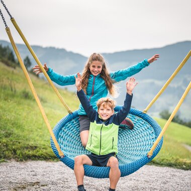 Kinder genießen eine Schaukel im Hochkönig, umgeben von grünen Wiesen und Bergen.  | © Hochkönig Tourismus GmbH