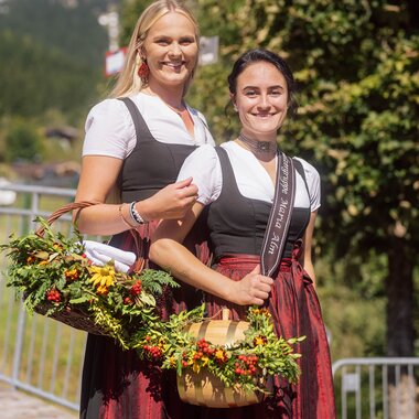 Zwei Frauen in Tracht mit Blumenkorb im Sonnenschein der Region Hochkönig. | © Hochkönig Tourismus GmbH