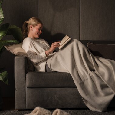 A young woman is sitting comfortably on the couch, covered up, reading a book. | © Karin Pasterer