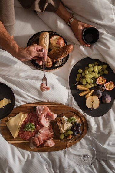 Ein Paar sitzt im Bett und frühstückt verschiedene Aufschnitte und Brot | © Karin Pasterer