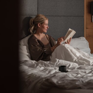 Eine junge Frau sitzt gemütlich im Bett und genießt ein Buch | © Karin Pasterer