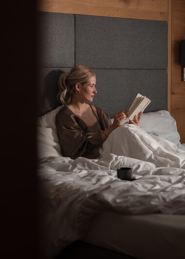 Eine junge Frau sitzt gemütlich im Bett und genießt ein Buch | © Karin Pasterer