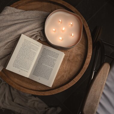 Nahaufnahme einer stimmungsvolle Kerze und einem offenen Buch auf einem Couchtisch | © Karin Pasterer