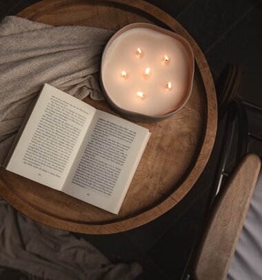 Nahaufnahme einer stimmungsvolle Kerze und einem offenen Buch auf einem Couchtisch | © Karin Pasterer