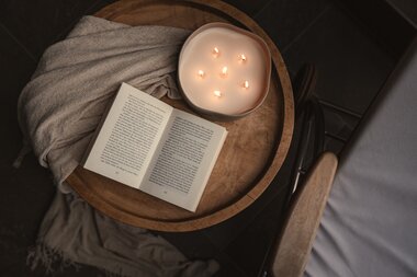Nahaufnahme einer stimmungsvolle Kerze und einem offenen Buch auf einem Couchtisch | © Karin Pasterer
